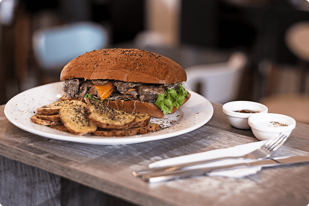 Restoran masasında, soslarıyla birlikte tabakta servis edilen, kızarmış patatesli gurme bir hamburger.